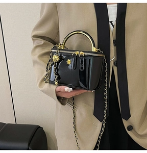 Detail of glossy black patent leather mini bag with gold floral clasp and chain