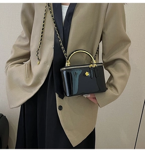 Detail of a black patent leather mini crossbody bag with gold floral hardware and chain