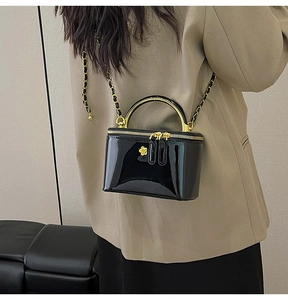 Detail of a glossy black crossbody bag with gold handle and woven chain strap