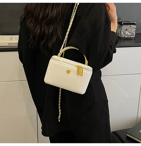 Detailed view of a white vanity case with gold handle and chain strap on a model