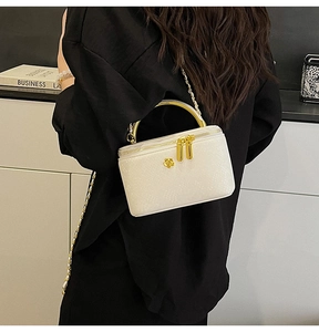 Detail of white snakeskin leather makeup bag with gold floral logo and metal handle