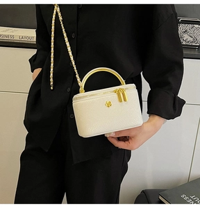 Detail of white mini vanity bag with gold flower emblem and metal chain strap