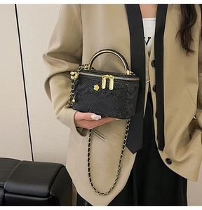 Detail of black snake pattern mini makeup bag with golden handle and chain strap