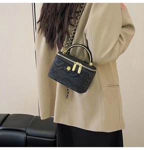 Detail of black snake pattern bag with golden handle and flower logo on shoulder