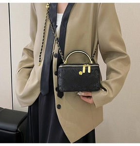 Detail of black snakeskin box bag with gold handle and floral zipper charm