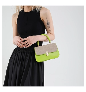 Detail of green leather handbag with woven flap and gold clasp on black dress