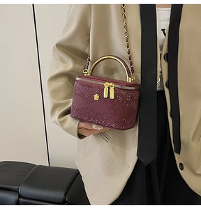 Detail of burgundy snakeskin texture bag with gold handle worn by a model in a suit