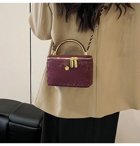 Detail view of burgundy snake-pattern crossbody bag with gold handle and flower pendant