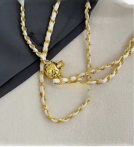 Detail of gold metal chain strap with woven white leather and decorative sphere buckle