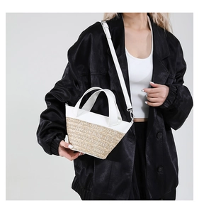 Detail of woven straw bucket bag with white leather straps and crossbody metal hardware
