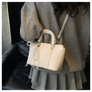 Close-up of cream leather handbag with delicate lace bow and pearl charm details