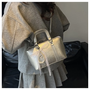 Detail of silver metallic handbag with lace trim, pearl charm, and round handle on leather