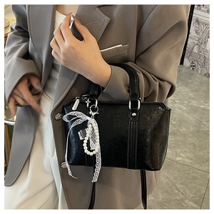 Detail of black faux leather bag with white lace bow and pearl pendant decoration