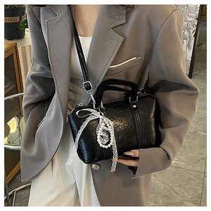 Detail of black textured leather handbag with white lace ribbon and beaded pendant charm