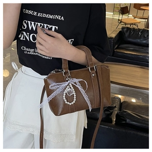 Detail of vintage brown leather bag with white lace bow and elegant pearl charm
