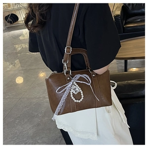 Detail view of brown leather bag with lace bow and pearl charm on a model