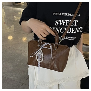 Detail of a brown leather shoulder bag with delicate white lace bow and pearl pendant