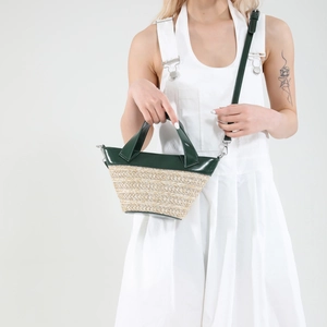 Woven straw bucket bag with green leather trim, featuring a top handle and shoulder strap