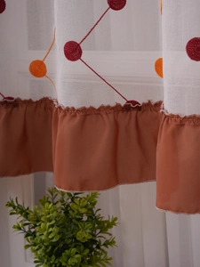 Detail of white semi-sheer cafe curtain featuring colorful embroidery and coffee ruffled hem