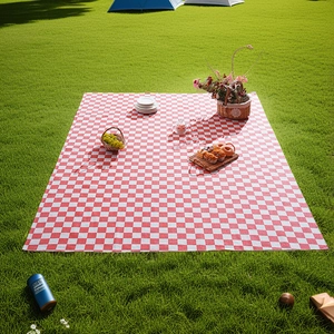 Outdoor red and white checkered picnic mat spread on green grass with picnic basket