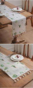 Detail of embroidered cactus pattern on linen table runner with white cotton tassels