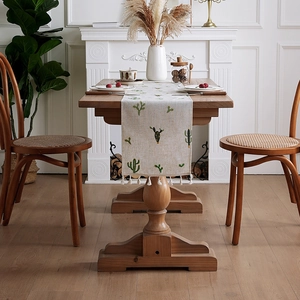 Linen table runner with green cactus embroidery and white tassel balls on wooden table