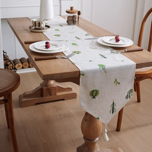 Linen table runner with green cactus embroidery and white tassels on a wooden table