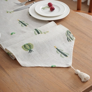 Linen table runner with cactus embroidery and white tassel fringe on wooden table