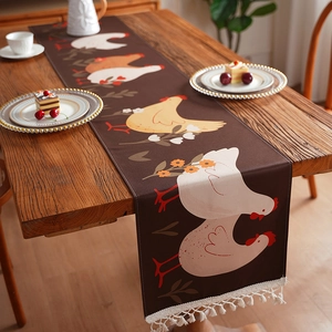 Waterdichte tafelloper met kippenprint en witte kwastjes op een rustieke houten tafel