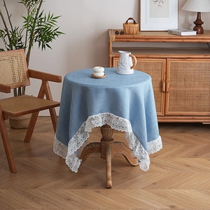 Dettaglio di tovaglia in lino blu con bordo in pizzo bianco su un tavolo tondo in legno
