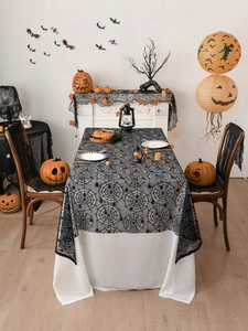 Close-up of black spider web lace tablecloth layered over white fabric for Halloween décor