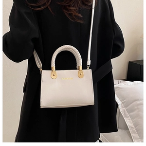 Detail einer weißen Handtasche mit geflochtenem Griff und goldenem Mode-Schriftzug
