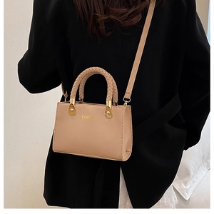 Detail der geflochtenen Griffe und goldener 'FASHION' Aufdruck auf einer beige Handtasche