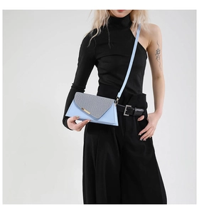 Sac bandoulière trapèze bleu clair avec rabat texturé et boucle dorée porté par un modèle