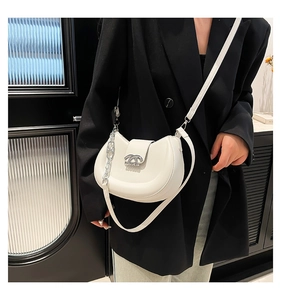 Detail der weißen Halbmond-Tasche mit Silberschnalle und Kette auf schwarzem Blazer