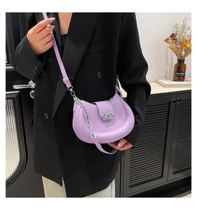 Detailansicht der lila Mondsichel-Tasche mit Silberkette und Logo über schwarzem Blazer