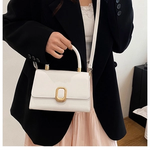 Petit sac carré en cuir blanc brillant avec boucle dorée sur blazer noir