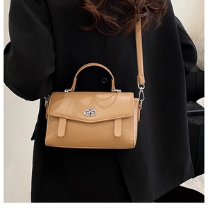 Detalle de bolso mensajero caqui con cierre giratorio plateado sobre un blazer negro