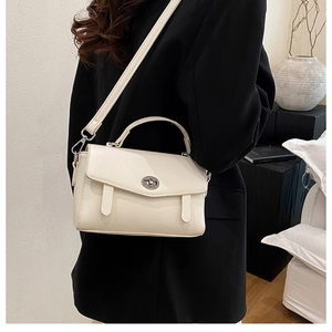 Detalle de bolso bandolera beige con cierre giratorio metálico sobre chaqueta negra