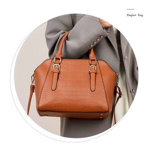 Detail of crocodile embossed leather handbag with gold metal feet and strap buckles