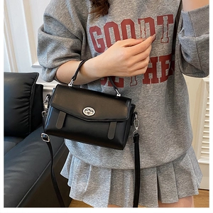 Detalle de bolso bandolera de cuero negro con cierre metálico giratorio plateado y asa