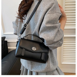 Detalle del bolso bandolera negro minimalista con cierre giratorio plateado y asa superior