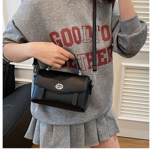 Detalle de bolso bandolera negro con cierre plateado y tiras decorativas en modelo