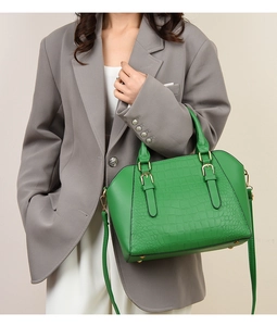Detailed view of green crocodile pattern tote with metallic buckle on a grey suit