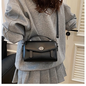 Detalle de bolso bandolera minimalista negro con cierre de giro ovalado en plata