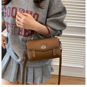 Bolso bandolera de cuero marrón con cierre giratorio plateado mostrado por una modelo