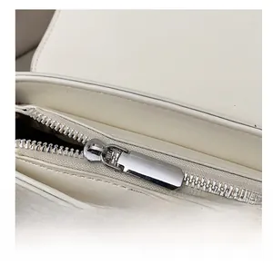 Primer plano de la cremallera de metal plateado y costuras del bolso de cuero blanco