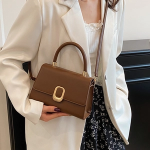 Sac à bandoulière carré marron avec fermoir doré porté sur une veste blanche