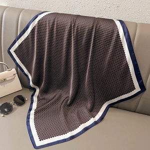 Detail view of silky square scarf with geometric pattern draped on a beige leather sofa