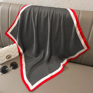 Detail of a red-bordered faux silk scarf with geometric patterns on a grey sofa